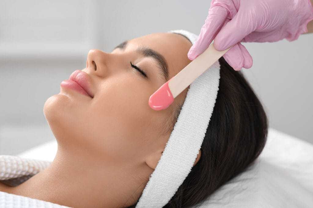Facial treatment in progress at a spa. Person receiving applied pink facial mask.