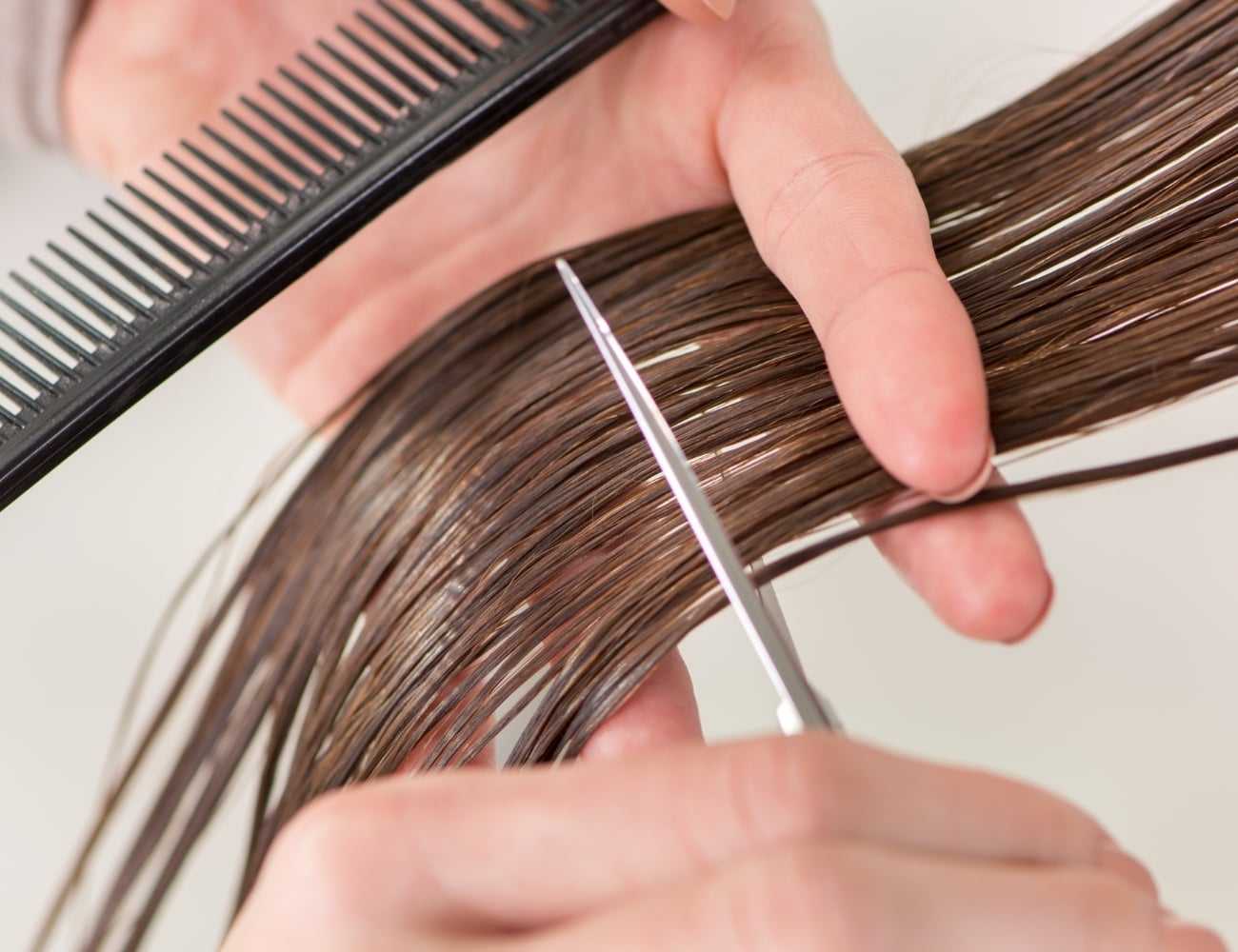 Cutting wet brown hair with a pair of scissors and a black comb.