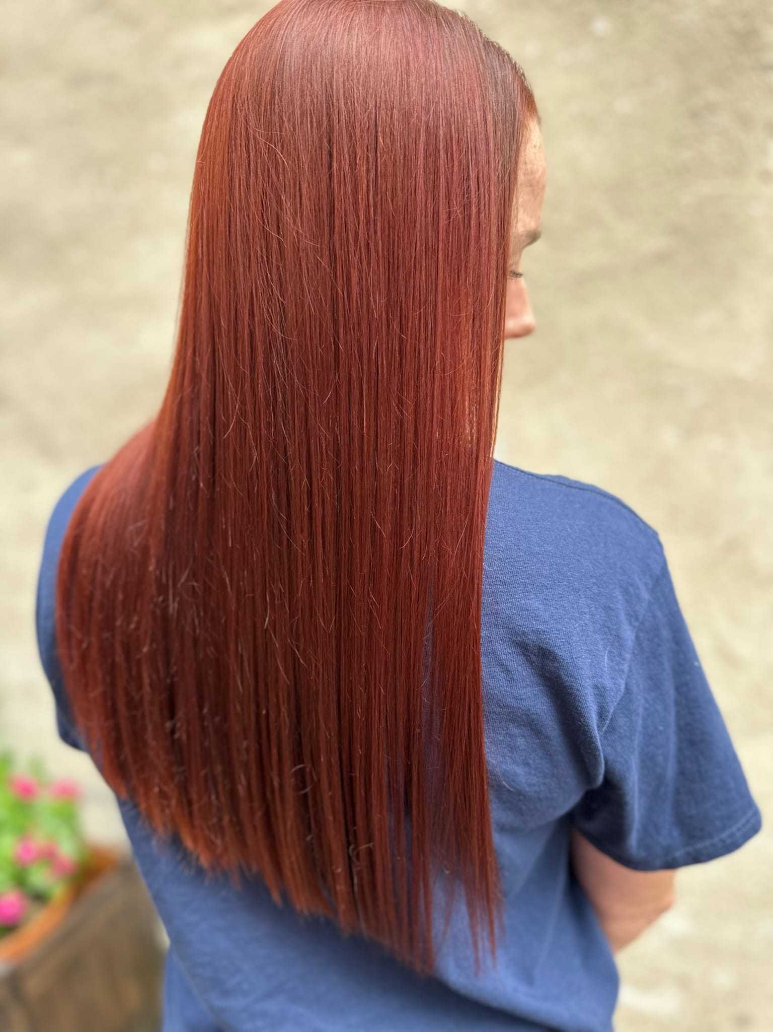 Woman with long, straight, auburn hair in a blue shirt, viewed from the back.