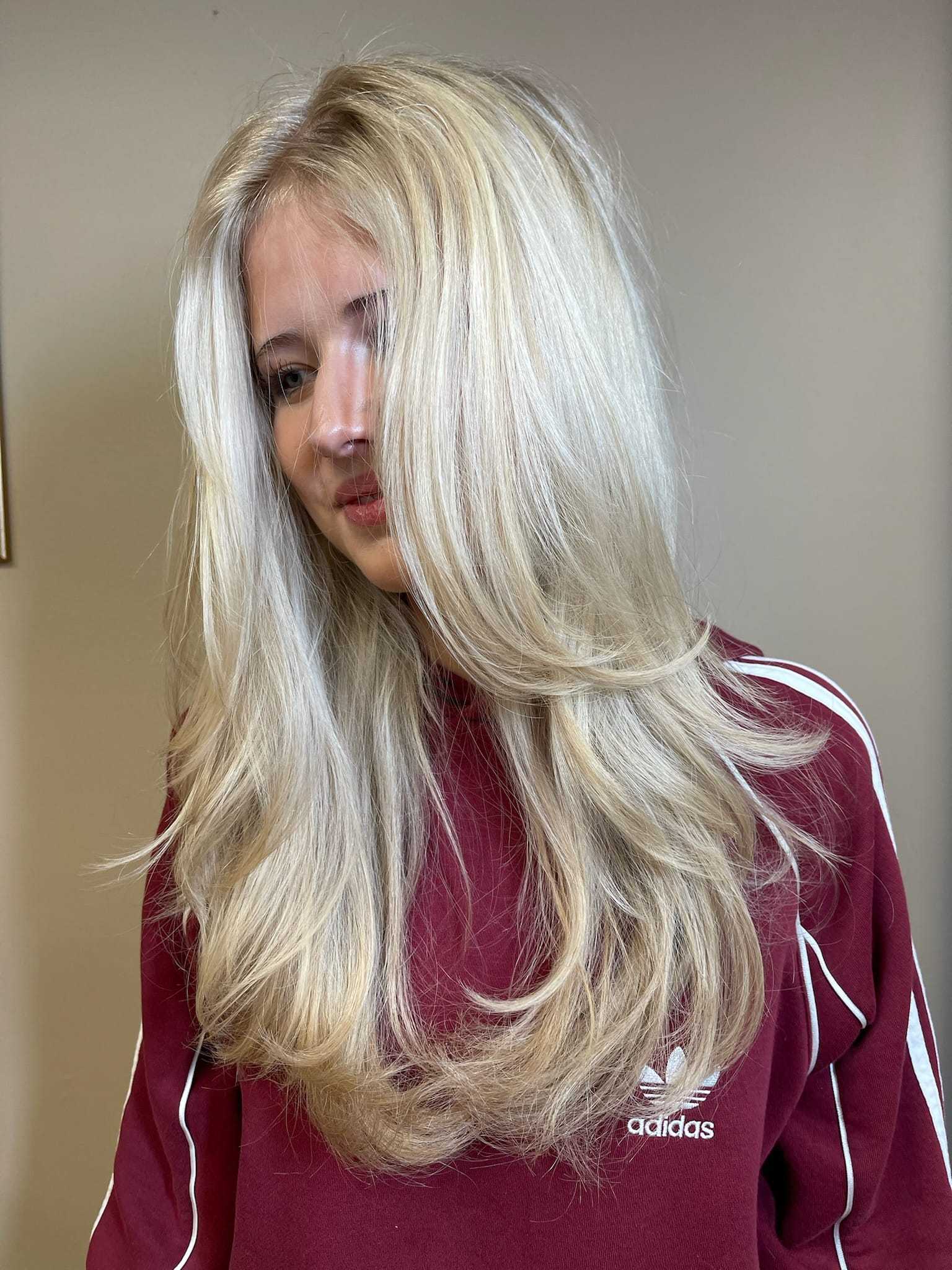 Blonde woman with long layered hair, wearing a maroon Adidas sweatshirt, looking down.