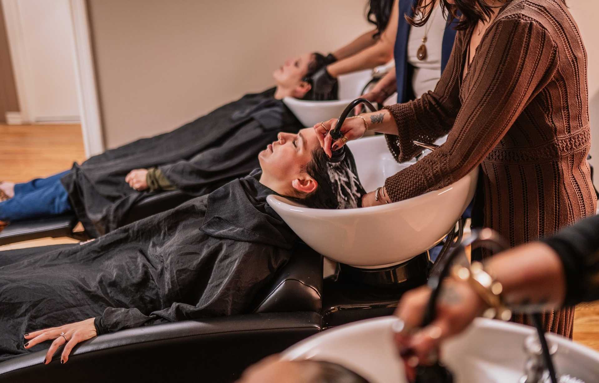 Women getting hair washed at salon sinks, beauticians attending with care.