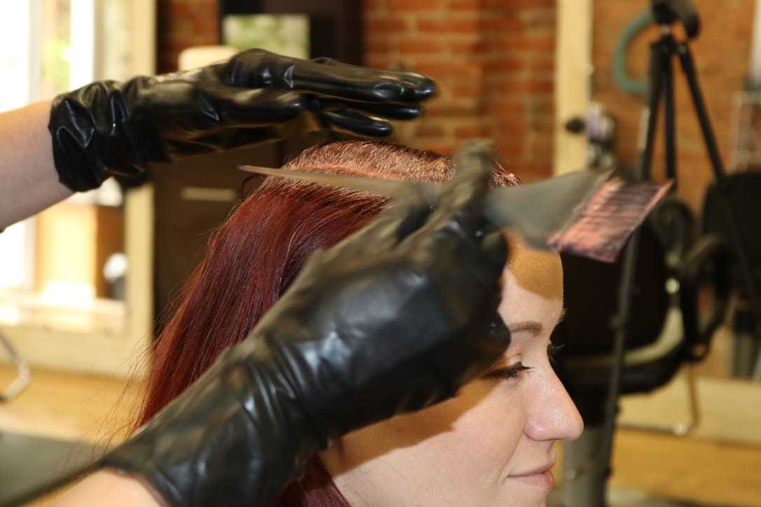 Hairdresser applying dye to client's red hair in a salon.