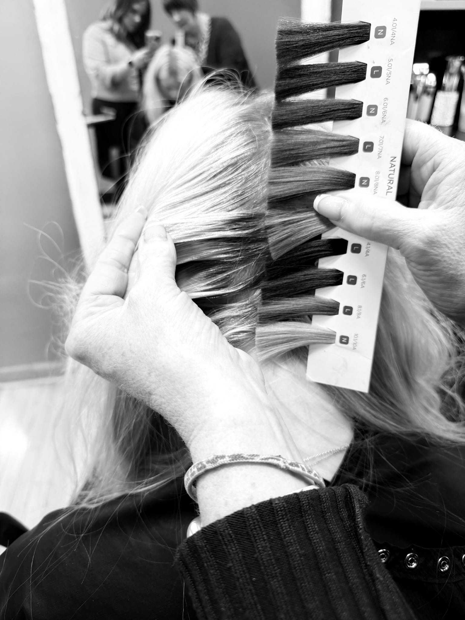 Hairstylist matching hair color swatches to client's hair in a salon.