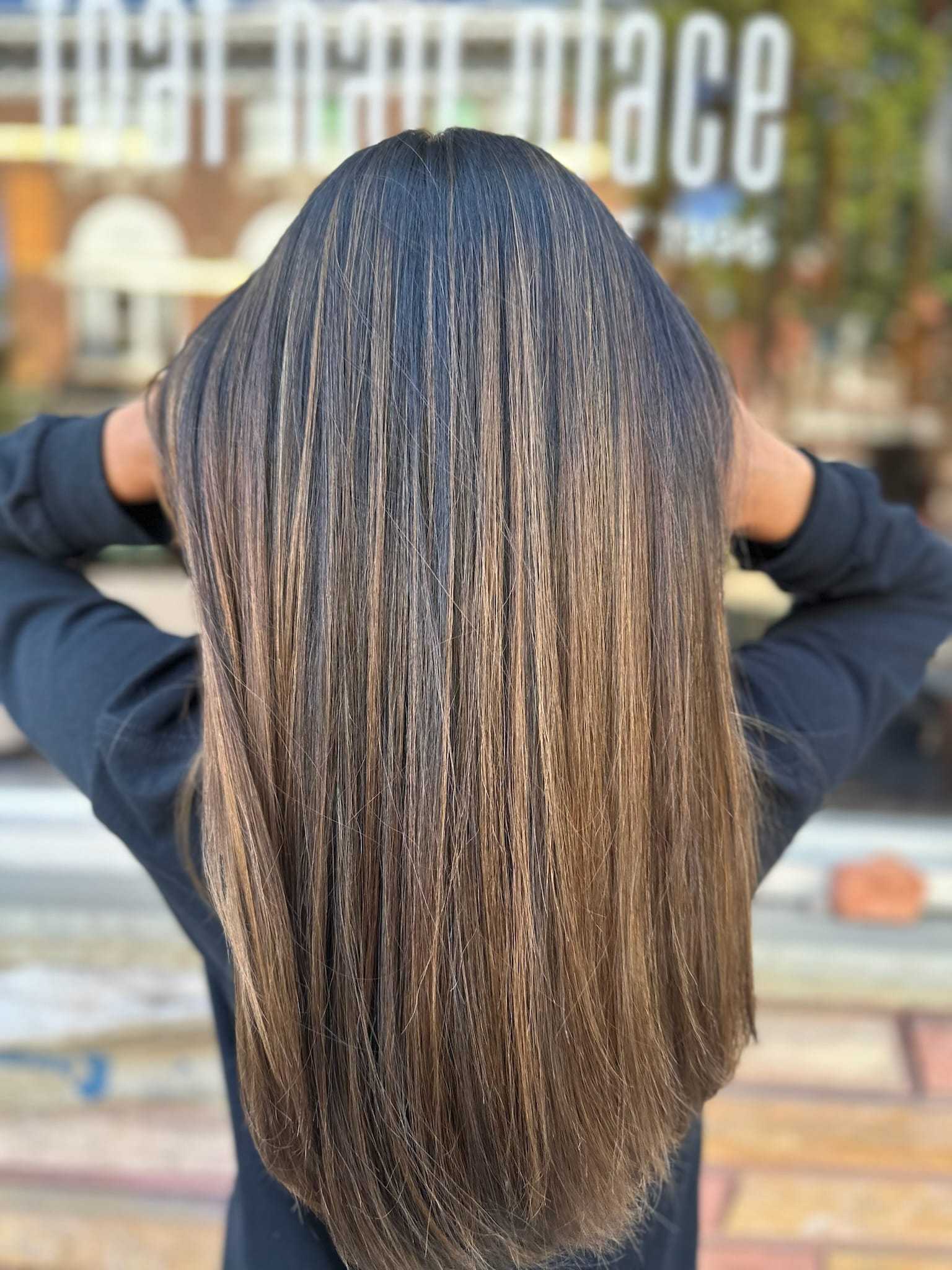 Long, straight hair with brunette and caramel highlights, hands touching both sides.