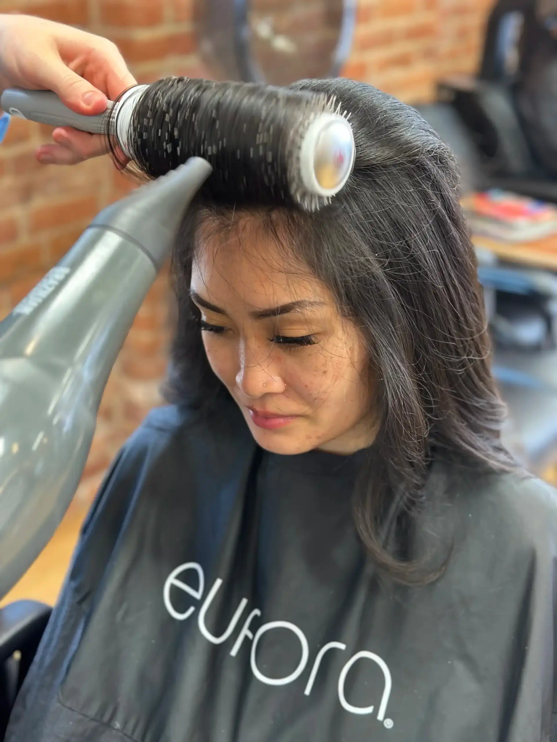 Woman getting hair blow-dried and styled with a round brush in a salon.