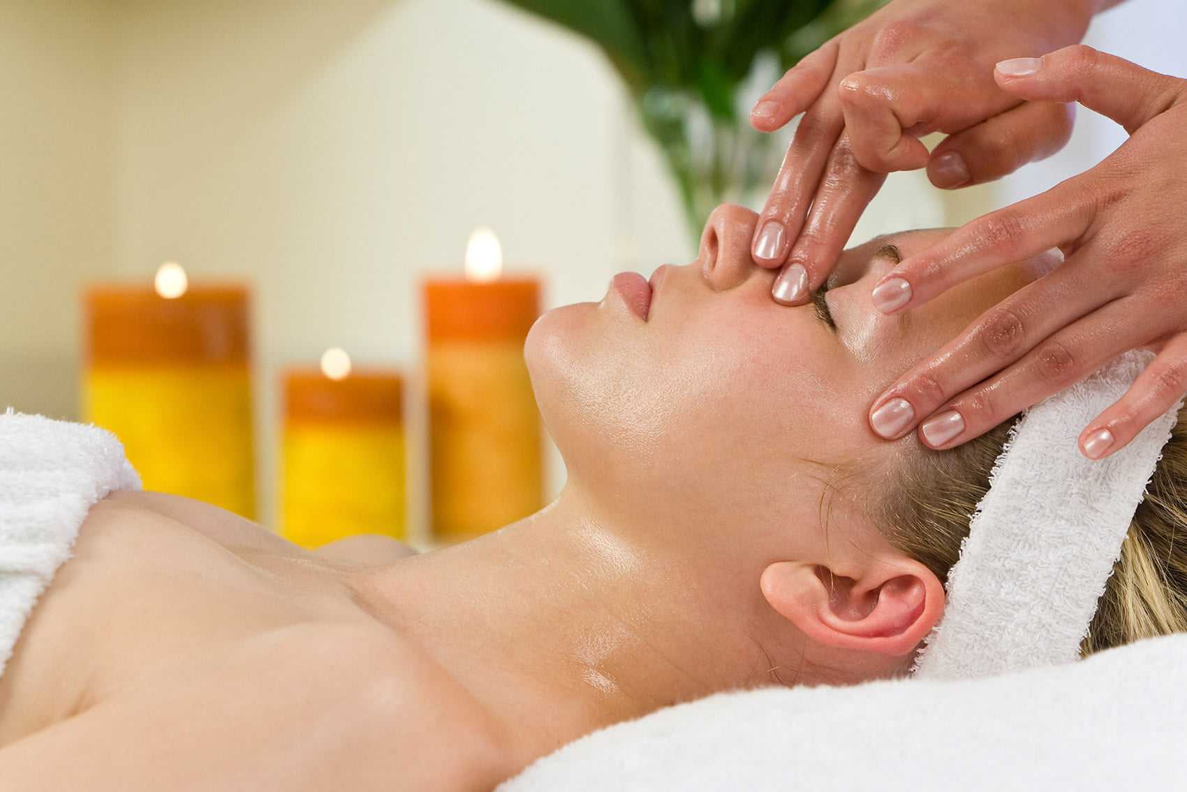 Person receiving a facial massage at a spa with lit candles in the background.