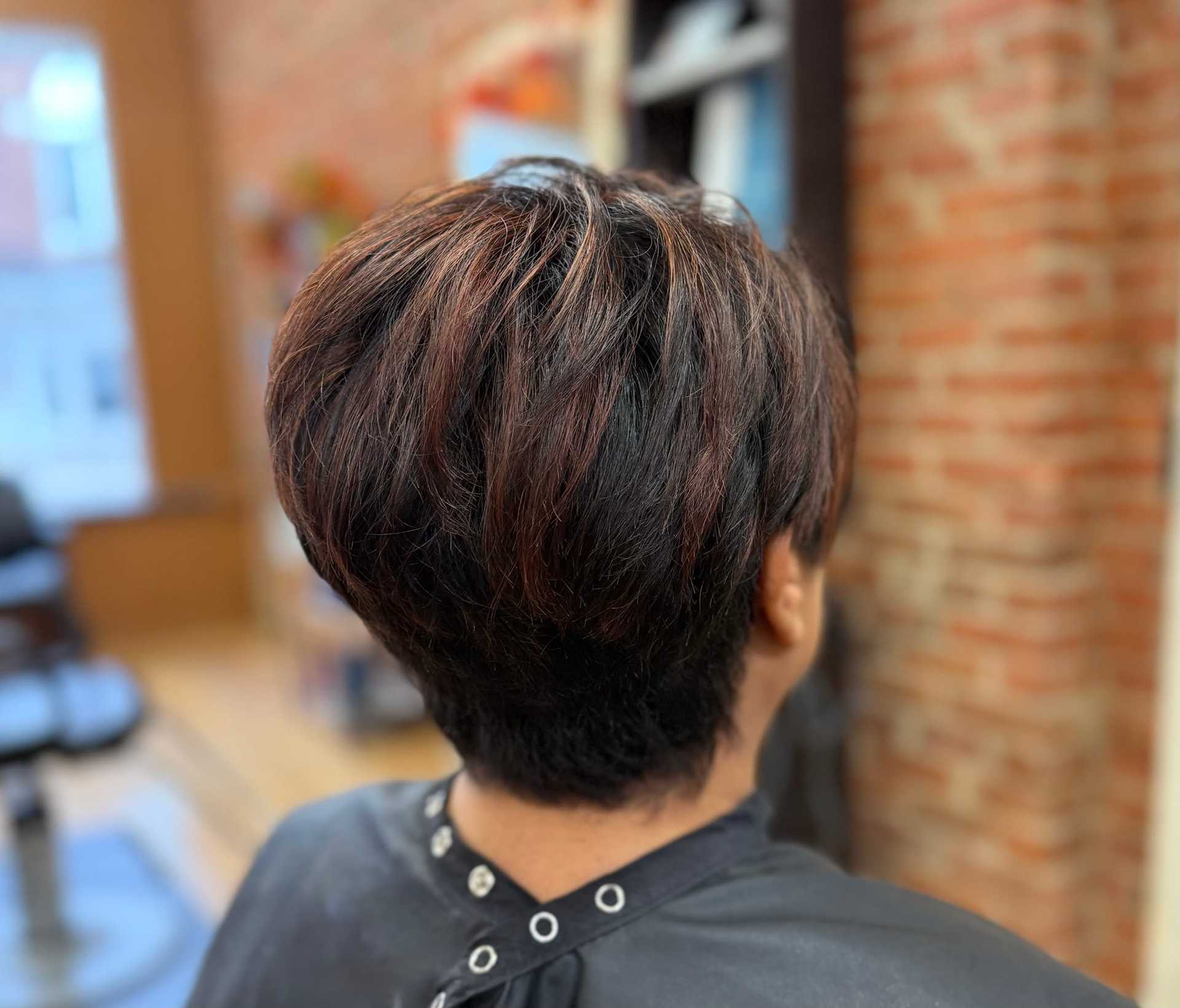Short-haired person in a salon chair, showcasing a stylish layered haircut with auburn highlights.