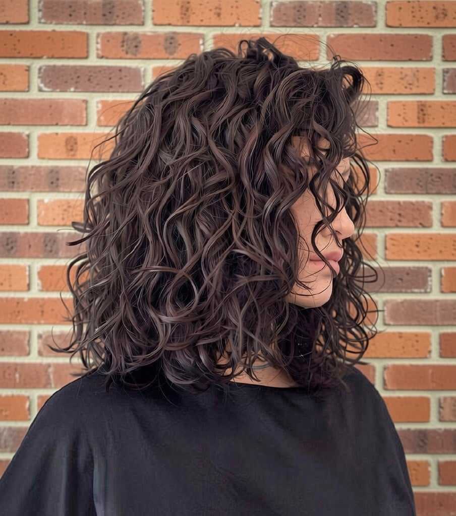 Woman with curly hair standing against a brick wall, wearing a black shirt.